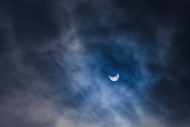 Güneş 'in tam tutulmasına yakın. Ay, güneş tutulması ve bulutlu dramatik gökyüzü ile güneşi kaplar. Doğa olayı.