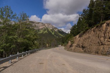 Sabahleyin Kanada, Alberta 'daki Banff Ulusal Parkı' nda orman boyunca uzanan boş viraj yolu. En güzel bakış açılarından biri. Ormanda manzaralı köy yolu.