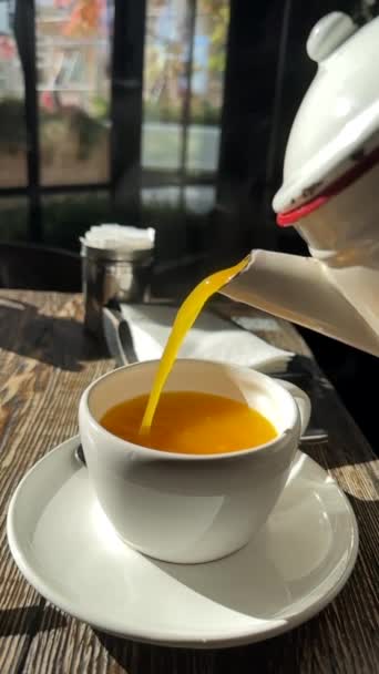 湯気のある熱いビタミンシーバソーン茶は 古い木製のテーブルの上に立っているソーサーとティーカップのティーポットからストリームで注ぎます 季節のインフルエンザや寒さの間に天然のホットドリンクの概念 スローモーション — ストック動画
