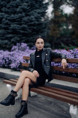 Genç ve güzel bir kadın, çiçek açan ağaçların ve çiçeklerin arka planında, parkta bir bankta oturur ve dinlenir..