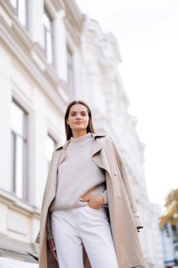 Pelerinli genç bir kadın binanın arka planında caddede yürüyor. Yakın çekim..