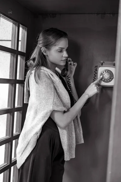 若い女性は公衆電話ブースで電話番号をダイヤルします 閉鎖だ 白黒の画像 — ストック写真