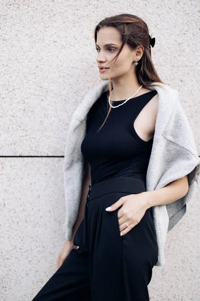 stock image Young pretty woman in black dress with necklace and sweater draped over the shoulders stands on street near building. Closeup.