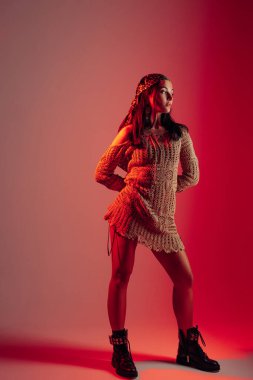 Genç kadın dantelli elbise ve bandanayla kırmızı arka planda kırmızı ışıkta poz veriyor..