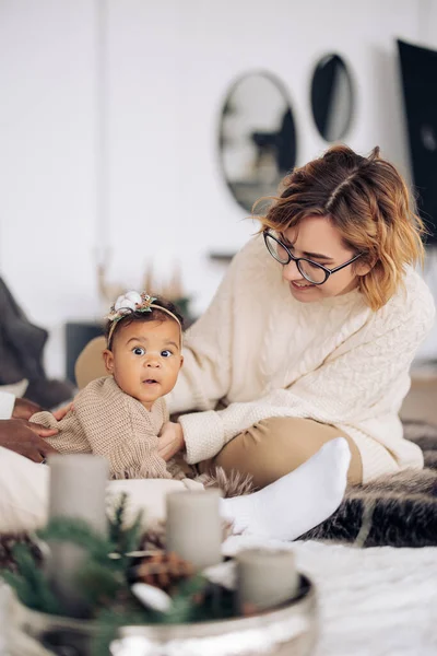 幸せな白人女性はクリスマスの装飾の背景に彼女の混合人種の赤ん坊の娘と遊ぶ 異人種間の家族と団結の概念 — ストック写真
