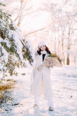 Neşeli genç bir kadın ormanda yürüyor. Güneşli bir kış gününde, karlarla kaplı çam ağaçları arasında. Ellerinde buketle..