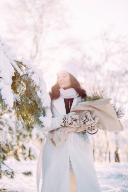 Neşeli genç bir kadın ormanda yürüyor. Güneşli bir kış gününde, karlarla kaplı çam ağaçları arasında. Ellerinde buketle..