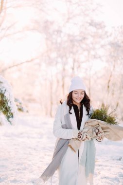 Mutlu, genç bir kadın, güneşli bir kış günü, elinde buketle karlarla ormanda yürüyor..