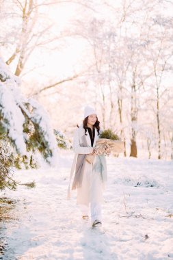 Mutlu, genç bir kadın, güneşli bir kış günü, elinde buketle karlarla ormanda yürüyor..