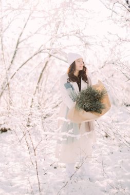 Mutlu, genç bir kadın, güneşli bir kış günü, elinde buketle karlarla ormanda yürüyor..