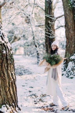 Mutlu, genç bir kadın, güneşli bir kış günü, elinde buketle karlarla ormanda yürüyor..