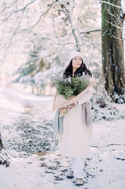 Mutlu, genç bir kadın, güneşli bir kış günü, elinde buketle karlarla ormanda yürüyor..
