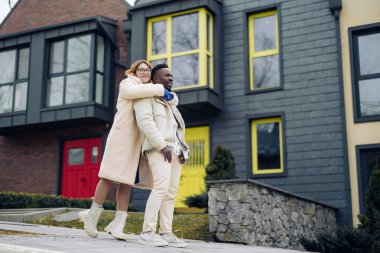 Young interracial couple embraces on street against background of houses. Concept of love relationships and unity between different human races.