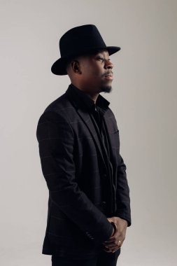 Young african man in suit and hat stands against gray background. Isolated image.