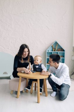 Young parents play with their toddler boy and build together pyramid tower at the children table. Educational and development games for babies.