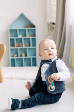 Happy toddler boy sits on floor and plays by toy in children's room.