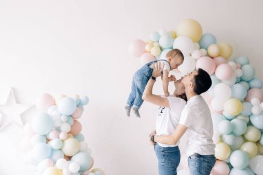 Happy parents have fun and play with their son celebrating first birthday of baby boy among a lot of colorful balloons. Celebration first birthday. Festive event.