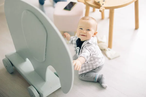 Happy toddler boy sits on floor and plays by toy in children's room.