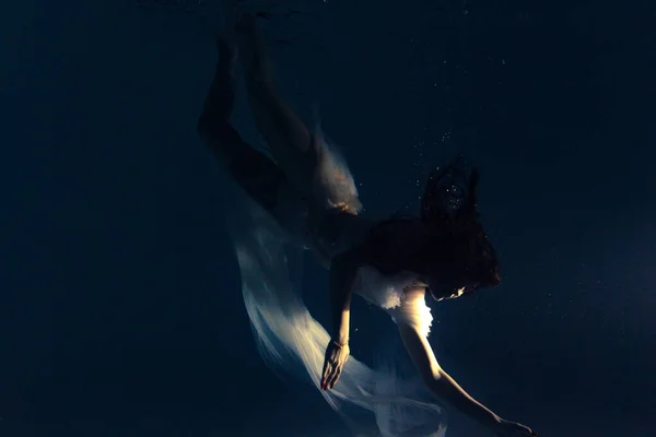白い飛行中の美しい女性の水中撮影透明なドレス太陽の光を介して水の中で泳ぐ 光の光線で水面を背景に幻想的な人魚 — ストック写真