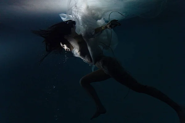 白い飛行中の美しい女性の水中撮影透明なドレス太陽の光で水の中でリラックス 光の光線で水面を背景に幻想的な人魚 — ストック写真