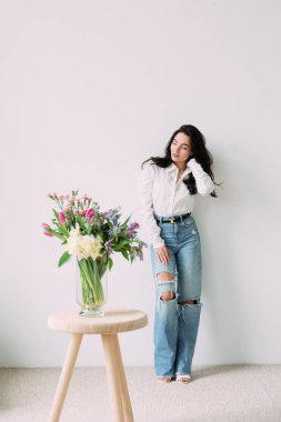 Masadaki güzel çiçek buketinin yanında duran düşünceli genç kadın. Anneler günü, doğum günü, yıldönümü, kutlama, tatil, selamlama, bayram etkinliği.