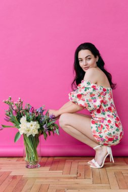 Genç bir kadın, çiçeklerin yanında vazonun içinde pembe fotografik arka planda poz veriyor. Doğum günü, yıldönümü, kutlama, bayram, selamlama, bayram etkinliği.