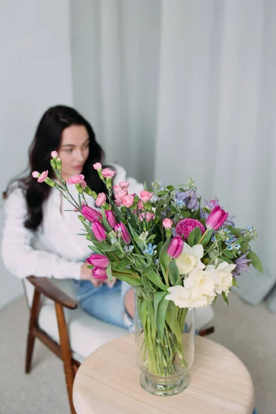 Gyönyörű Virágcsokor Van Asztalon Karosszékben Ülő Fiatal Elgondolkodtató Hátterével Szemben — Stock Fotó