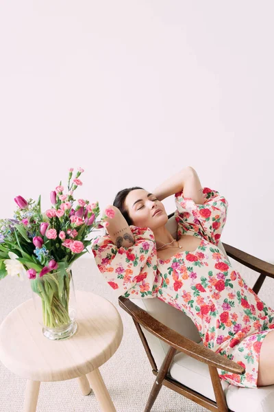Fiatal Álmodozó Karosszékben Csukott Szemmel Váza Mellett Gyönyörű Virágcsokorral Asztalon — Stock Fotó