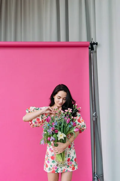Молодая Женщина Стоит Студии Исправляет Цветы Вазе Розовом Фотографическом Фоне — стоковое фото
