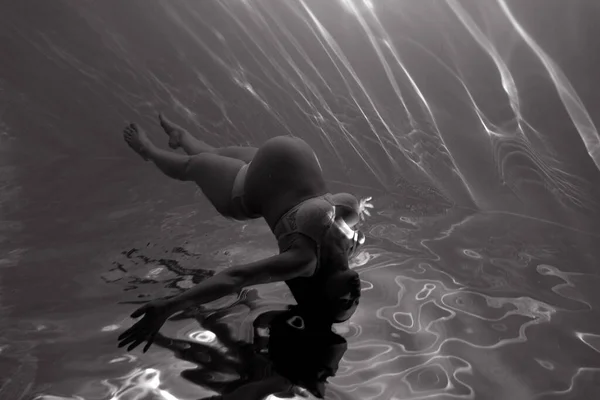 美しい妊婦の水中撮影水の中で日光浴を介して泳ぐ 光の光線と水の背景にファンタジー人魚 白黒の画像 — ストック写真