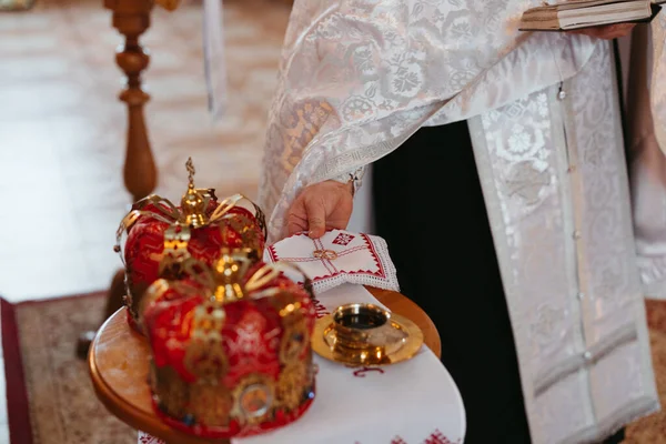 在乌克兰东正教教堂举行的婚礼上 牧师在红色婚冠的背景下 用绣花毛巾戴着两个金戒指 — 图库照片