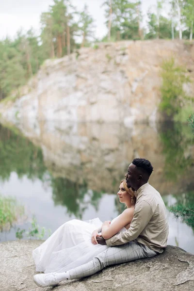 Ευτυχισμένο Διαφυλετικό Ζευγάρι Νεόνυμφων Κάθεται Βράχο Και Αγκαλιάζει Όμορφο Φόντο — Φωτογραφία Αρχείου
