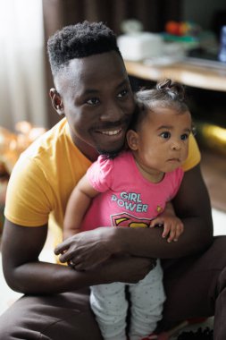 Genç Afrikalı bir adam, odadaki ırklar arası evlilikten olan küçük kızıyla oynuyor. - Yakın çekim. Irklar arası aile kavramı.