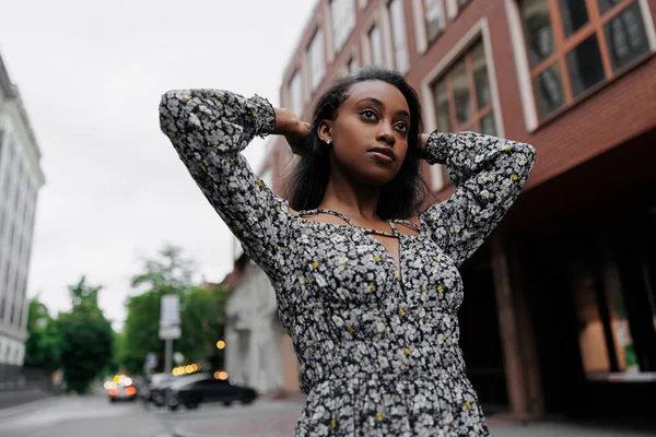 stock image Young african pensive woman in summer dress walks in city against background of building. Bottom view.