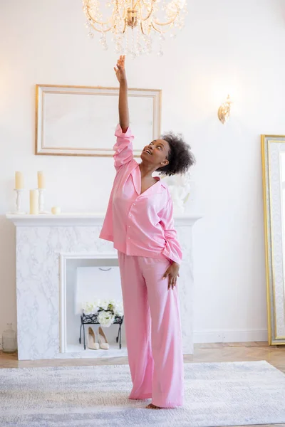 Fiatal Afrikai Örömteli Rózsaszín Pizsamában Szórakozás Kinyújtja Kezét Hogy Csillár — Stock Fotó