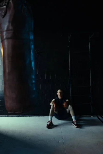 运动后戴拳击手套的疲惫拳击手在黑暗的体育馆休息 — 图库照片