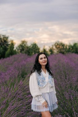 Genç esmer kadın gün batımının arka planında çiçek açan lavanta sıralarının arasında yürüyor ve eğleniyor..