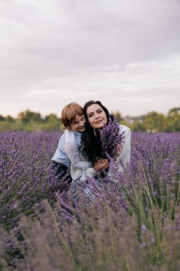 Neşeli anne ve oğul oturmuş, gökyüzünün arka planında çiçek açan lavantalar arasında eğleniyorlar..