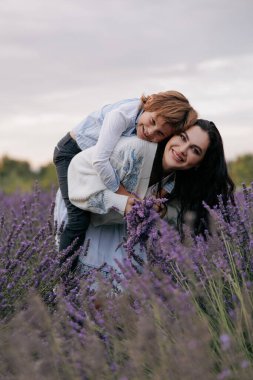 Gülen anne ve oğul gökyüzünün arka planında çiçek açan lavantalar arasında eğleniyorlar..