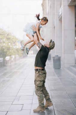 Savaştan dönen Ukraynalı asker küçük kızıyla tanışıyor ve neşeli bir şekilde çocuğu fırlatıyor. Ukrayna 'da savaş. Rus ordusu Ukrayna 'yı işgal etti. Savaş ve çocuklar.