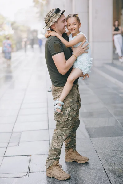 Ukrainian soldier returning from the war meets his little daughter and joyful embraces her. War in Ukraine. Russian military invasion in Ukraine. War and children.