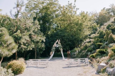 Güzel peyzaj bahçesinde düğün seremonisi şık bir düğün kemeriyle süslenmiş taze beyaz güller ve yanında beyaz banklar. Düğün, kutlama, etkinlik, romantik tarz. Taşra düğünü