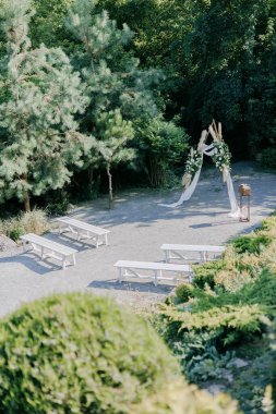 Güzel peyzaj bahçesinde düğün seremonisi şık bir düğün kemeriyle süslenmiş taze beyaz güller ve yanında beyaz banklar. Üst görünüm.