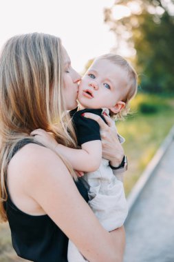 Parkta oğlunu öpen genç bir annenin portresi. Yakın plan..