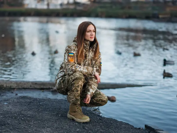 Ukrainian woman soldier resting in park during vacation near lake. Women and war. War in Ukraine. Russian military invasion. Translation from Ukrainian: Armed Forces of Ukraine, surname.