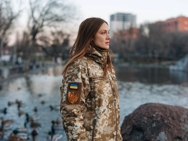 Ukrainian woman soldier walking in park during vacation near lake. Women and war in Ukraine. Russian military invasion. Translation from Ukrainian: Armed Forces of Ukraine, surname.