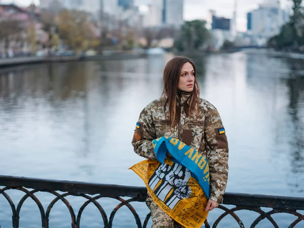 Ukrainian woman soldier holding flag with signatures of Ukrainian warriors and resting in park in vacation. Translation from Ukrainian: Armed Forces of Ukraine, Glory to Ukraine, surname.