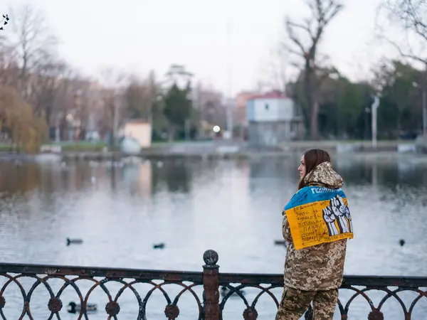 Ukrainian woman soldier holding flag with signatures of Ukrainian warriors and resting in park in vacation. Translation from Ukrainian: Glory to Ukraine.
