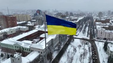Ukrayna 'nın rüzgâr bayraklarında kışın Dinyeper şehrinin ve karlı caddenin arka planında kar yağışı sırasında kuş bakışı bir bakış açısıyla dalgalanıyor. Yolların ve karla kaplı şehrin hava aracı görüntüsü. Ukrayna bayrağı.