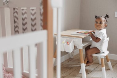 Çocuk odasında oynayan melez bir kız çocuk mobilyalarının yanında oturuyor. Afro-Kafkasyalı küçük kız. Irklar arası aile kavramı. Yakın plan..